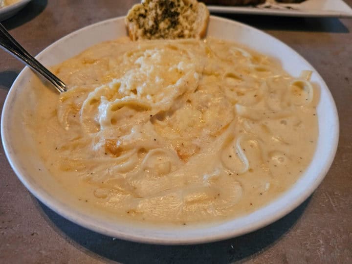 Fettuccine alfredo in a white plate with a piece of bread and spoon