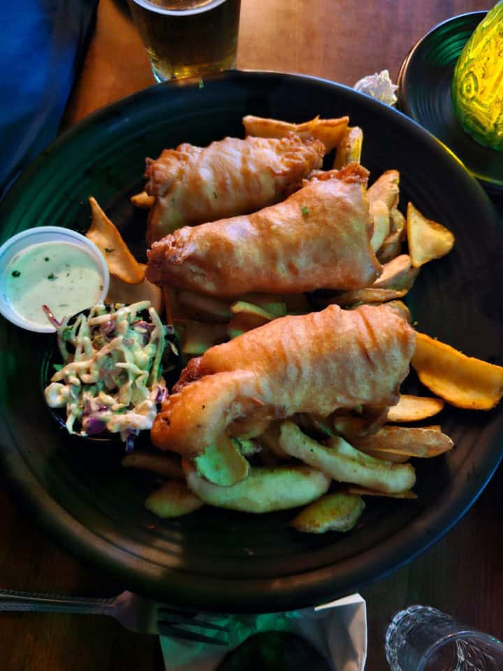 Fish and chips on a dark plate next to a beer