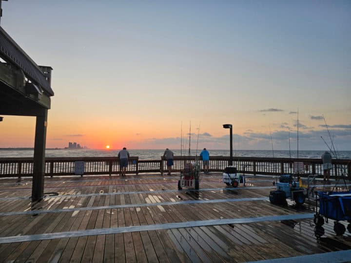 people fishing on the rail of the pier with sunrise in the background