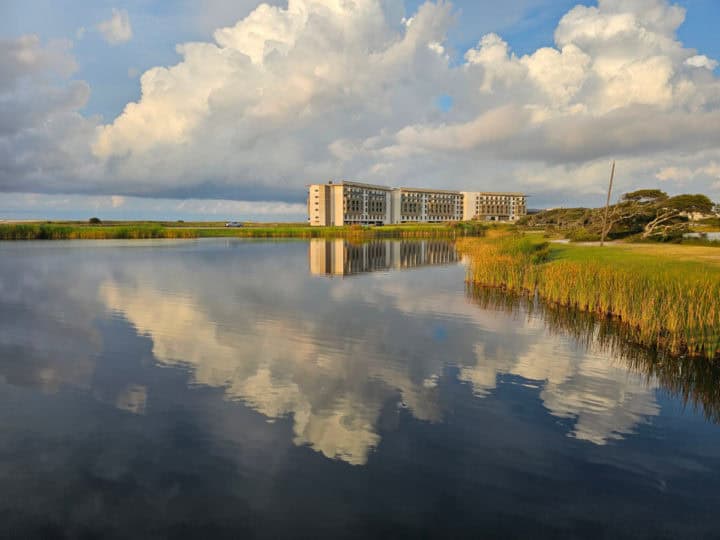 Gulf State Park lodge in the background reflected onto Lake Shelby with clouds and grass