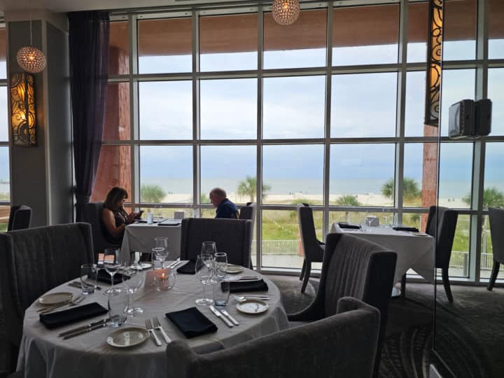 two people sitting at a table with floor to ceiling windows next to them looking out to the Gulf of Mexico