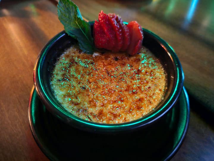 Creme brulee in a dark bowl garnished with strawberries