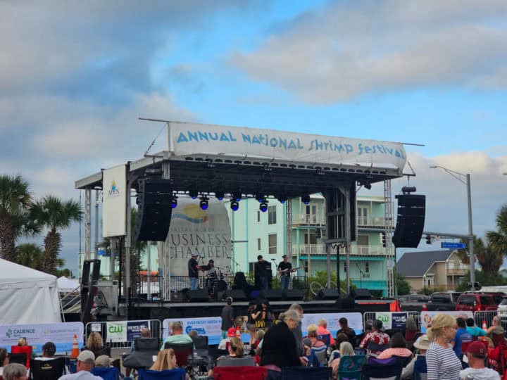 Annual National Shrimp Festival sign over an outdoor stage with people sitting watching live music