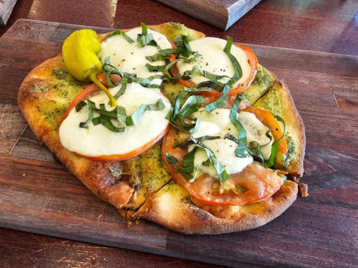 margherita flatbread with basil, tomato, and mozzarella cheese on a wooden board.