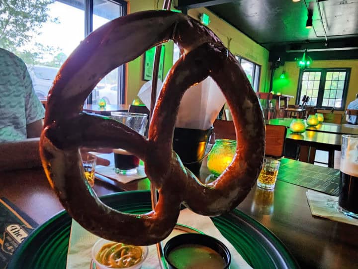 Giant pretzel on a hook above a green plate with mustard and beer cheese dip