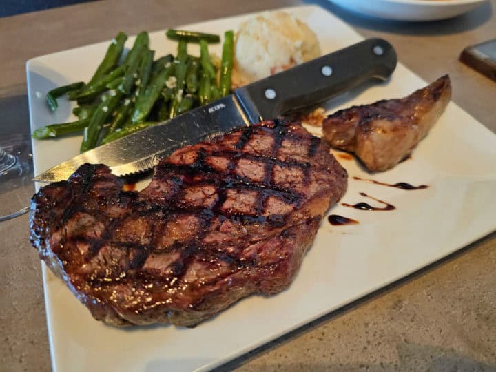 Ribeye steak on a white plate with mashed potatoes and green beans