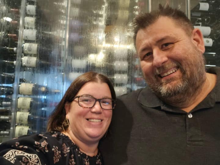 tammilee and john in front of a glass wine cabinet