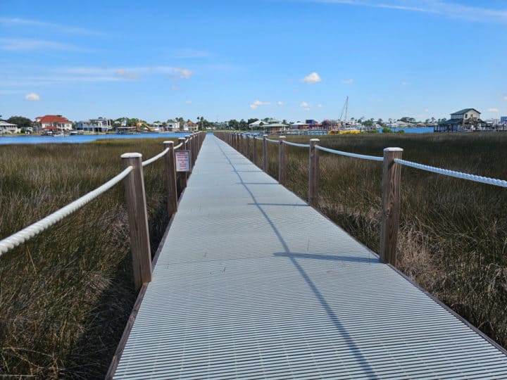 walkway through marsh area with sailboat in the distance