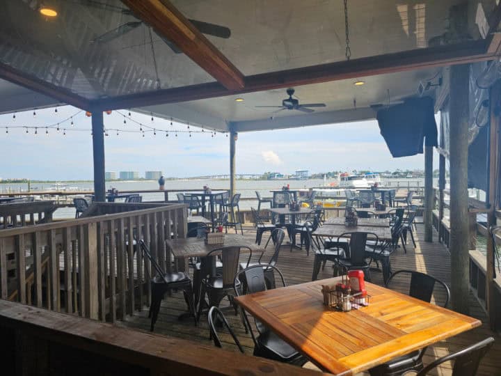 Tables and chairs on a covered eeck with a view of the water. 