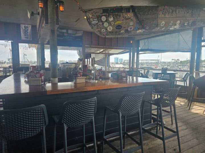 Bar with chairs next to a boat hanging from the ceiling and views out to the water. 