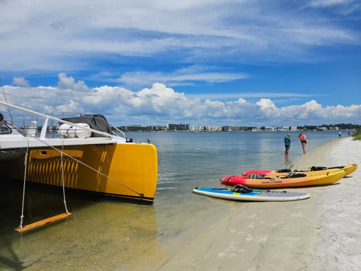 yellow front of the sailboat with a swing hanging down. Kayaks and paddleboards on the beach. 