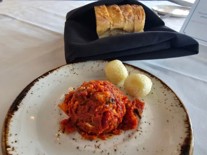 tomato chutney and butter balls on a white plate next to a basket of bread