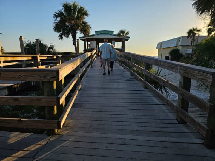 people walking on boardwalk towards pam trees and beach entrance