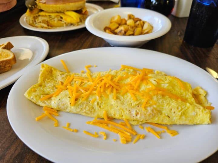 cheddar cheese omelet on a white plate next to a bowl of breakfast potatoes