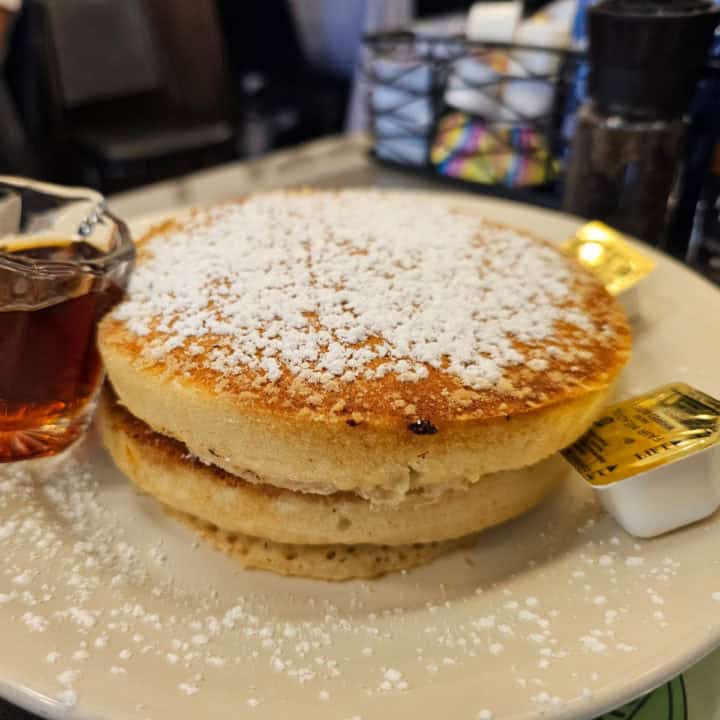 two fluffy pancakes on a white plate with syrup and buter