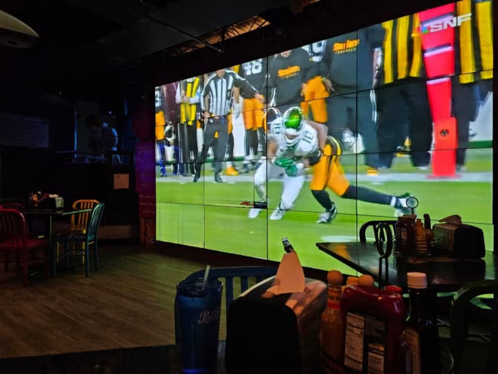 football playing on a giant flatscreen television near restaurant tables