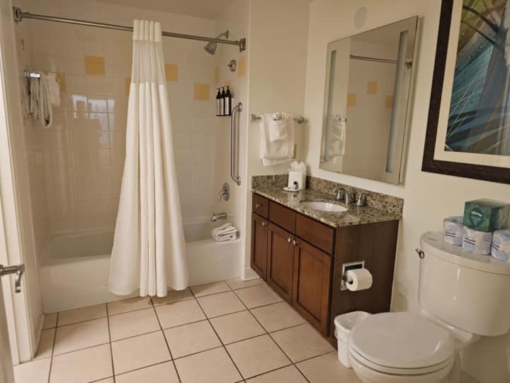 Shower and tub with a white shower curtain, single sink and mirror next to a toilet