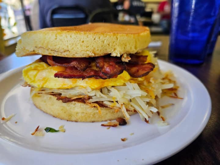 egg bacon hashbrowns and cheese between two pancakes on a white plate