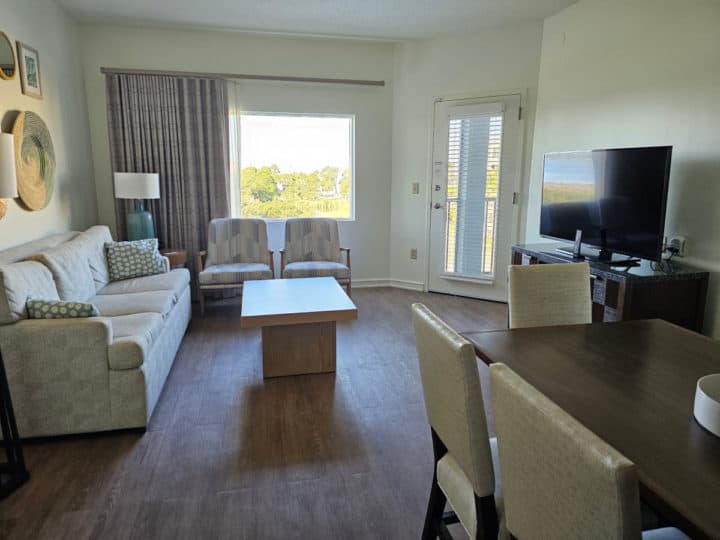 white couch under coastal art next to two chairs and a table. dining room table in the corner with white chairs