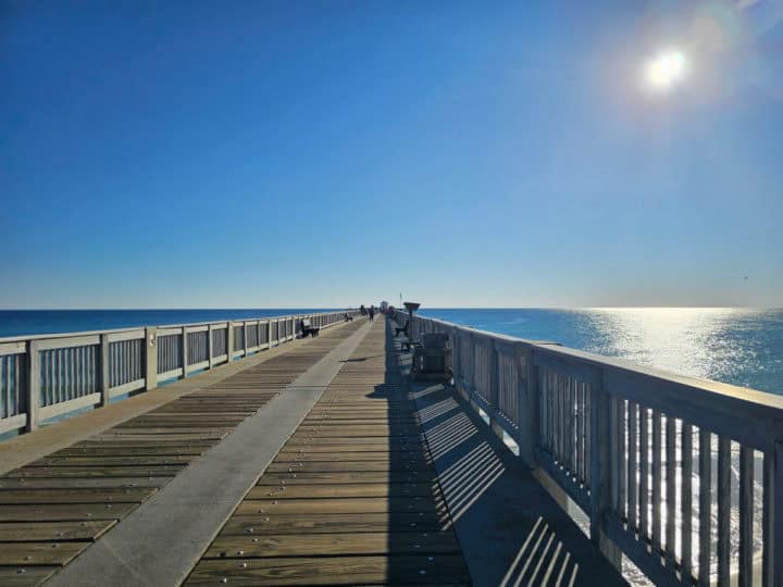 looking down the pier with the sun shining on the water