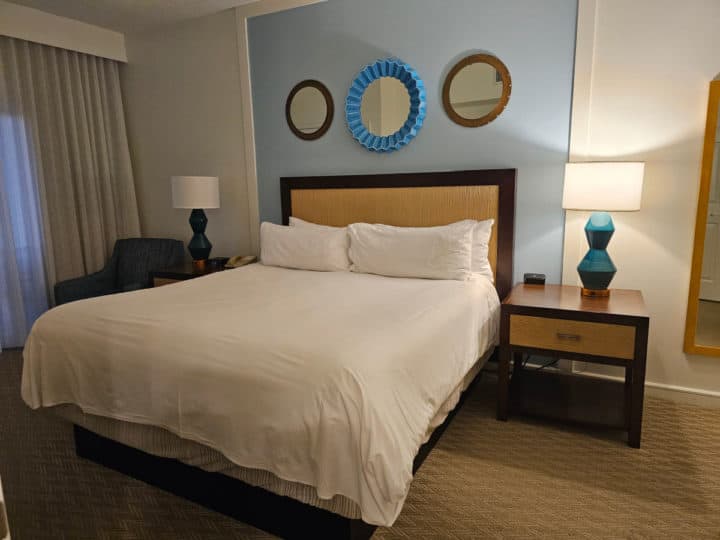 King size bed with white linens, two nightstands with lamps, and coastal blue background wall