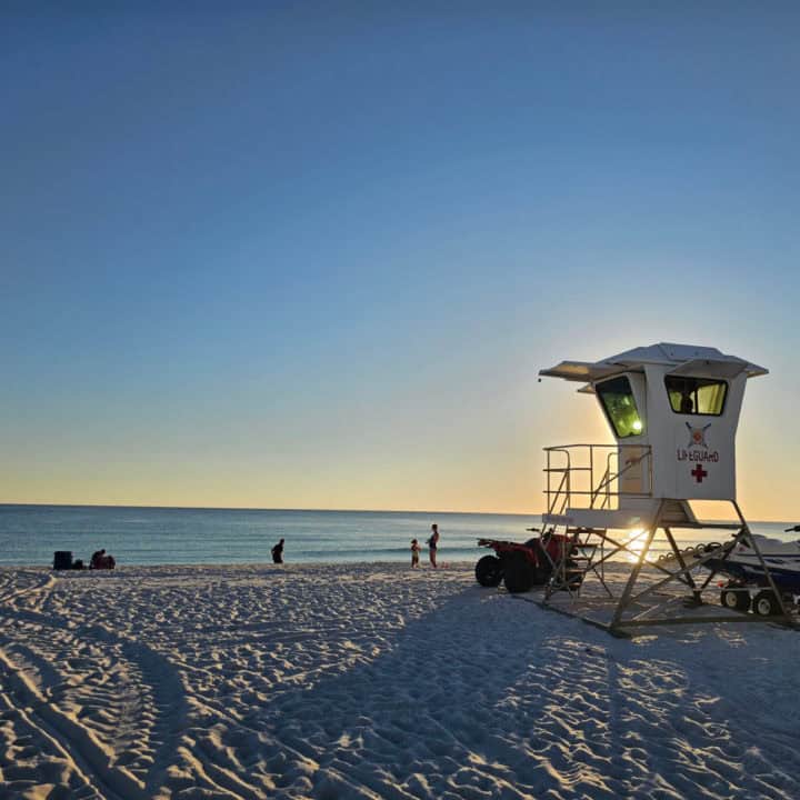 Lifegaurd stand lit up by the sunset with people playing on the beach by the water