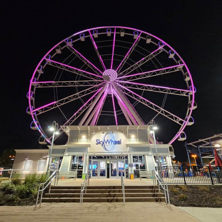 SkyWheel lit up purple at night above the SkyWheel entrance with glass doors