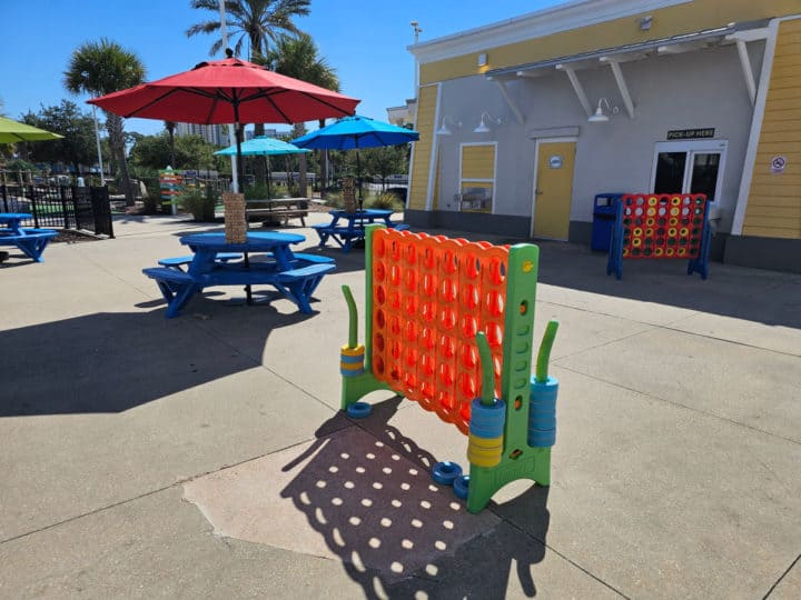 large connect four game next to tables with umbrellas and a snack shop