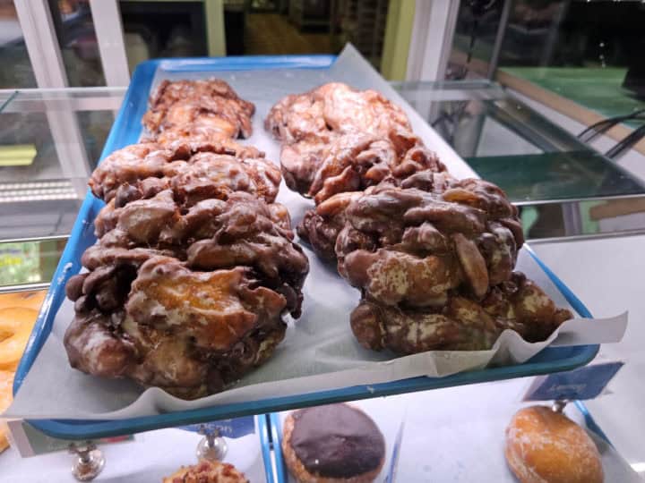 Apple fritters on a tray in a display case with donuts