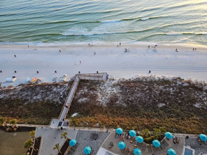 Looking down on pool umbrellas, a boardwalk leading out to the white sand beach and the Gulf of Mexico