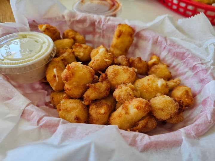 Cheese curds next to a container of ranch in a paper lined basket