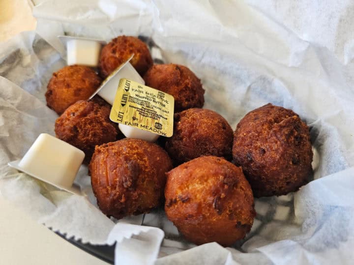 Hushpuppies with small containers of butter in a paper lined basket