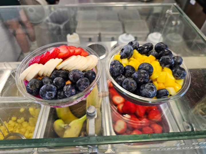 Two fruit bowls on a glass counter with fruit in buckets below them