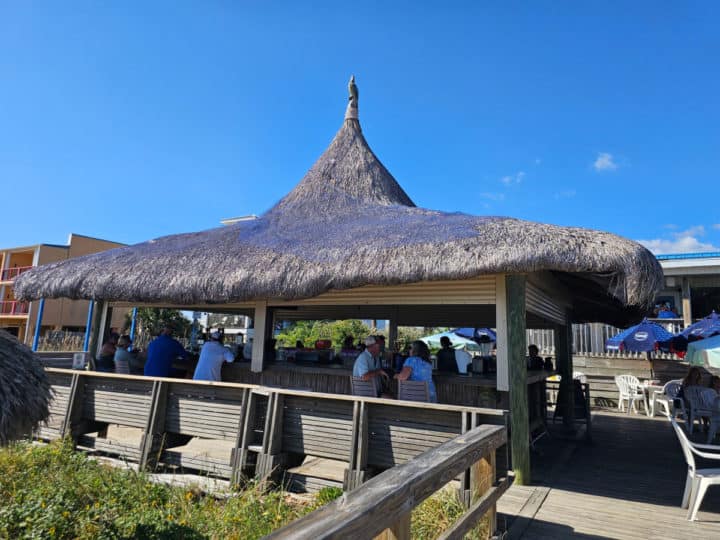 thatch covered tiki bar with people sitting at stools next to the bar