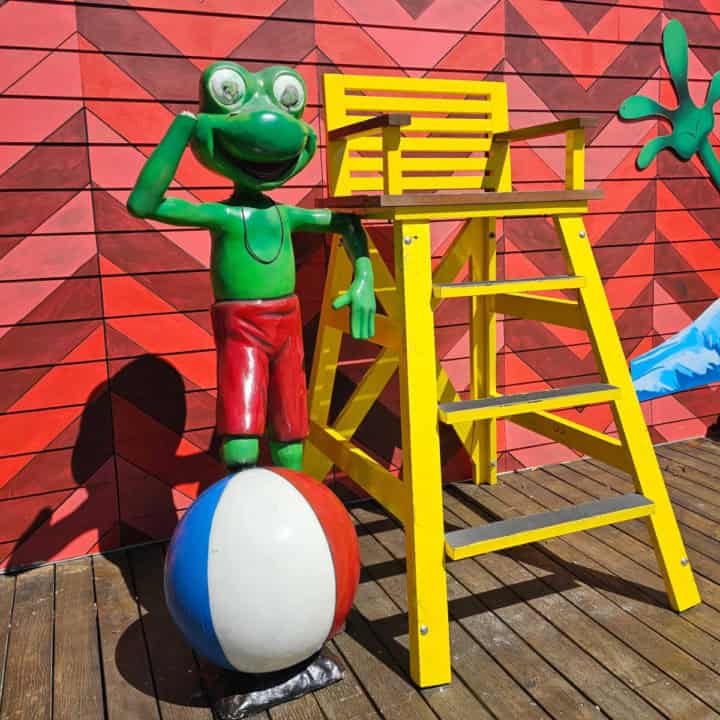 Green frog statue standing on a beach ball next to a yellow lifeguard stand at Senor Frogs