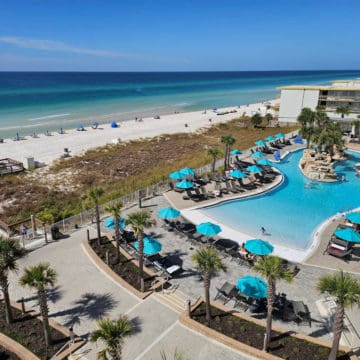 Looking down over a pool and lazy river, palm trees, and the beach along the Gulf of Mexico