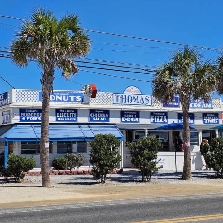 Blue and white Thomas donuts and snacks building behind a couple of palm trees