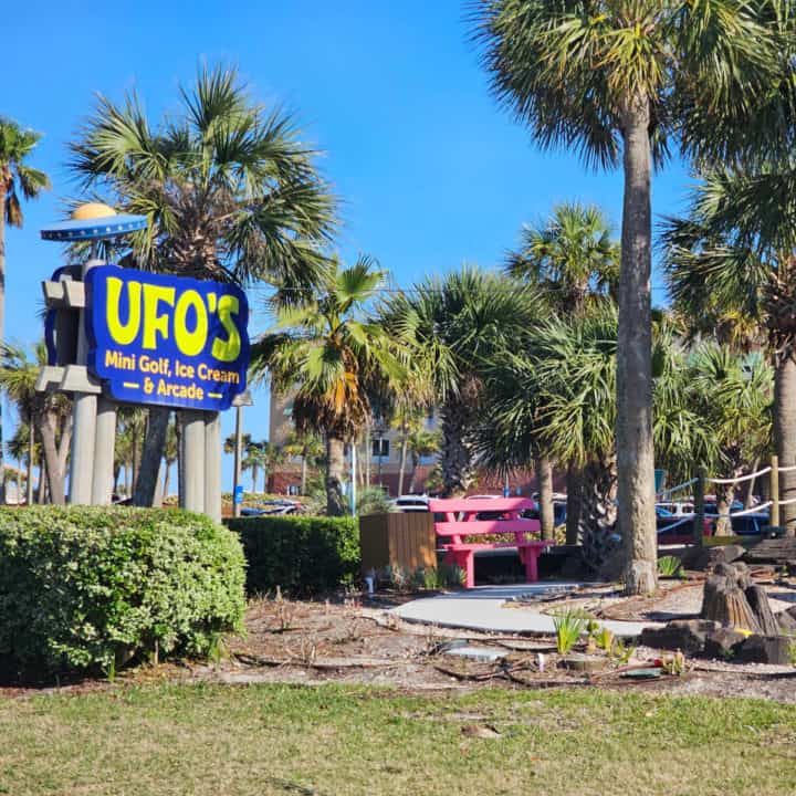 UFO's mini golf sign with a spacecraft on it next to a pink bench and palm trees