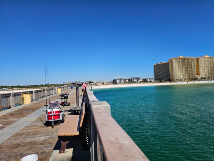 Fishing pier with fishing rods and a cooler looking out to the blue waters of the gulf and sandy beach