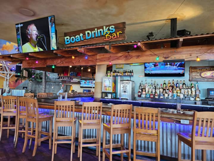 Indoor bar with tall bar stools, boat drinks bar sign, and jimmy buffet on the tv