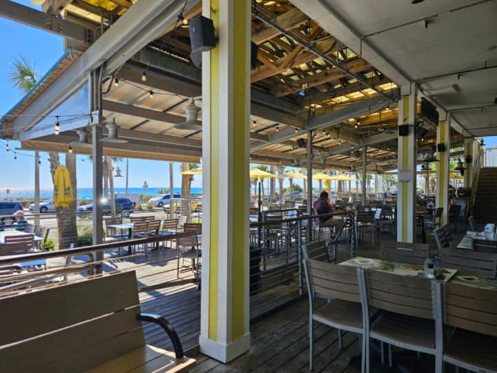 Outdoor seating with tables and chairs under a covered awning looking out to the Gulf of mexico 