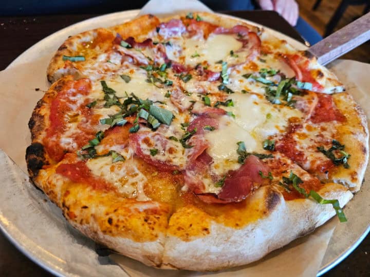 Pizza with proscuitto and cheese, basil on a parchment lined baking pan