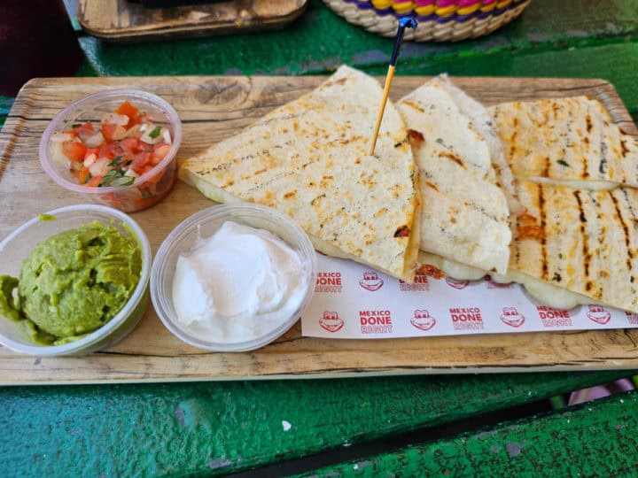 quesadilla triangles on a Senor frog paper lined board with salsa, guacamole, and sour cream