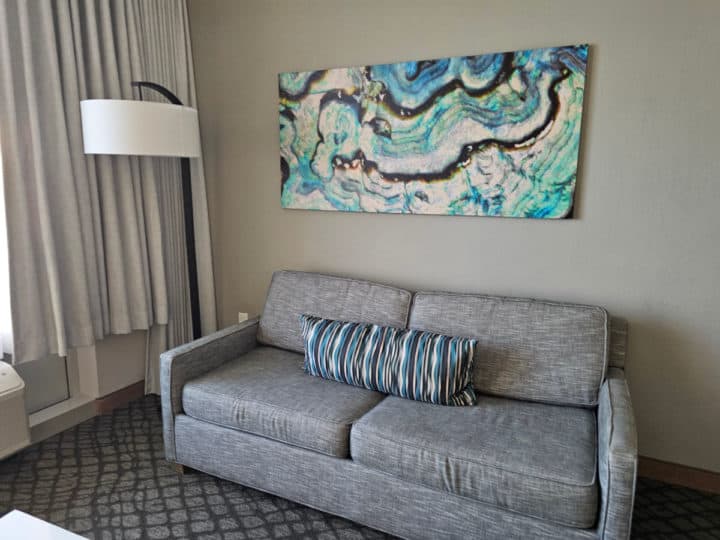 double couch under a tropical print next to a lamp