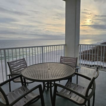 Table and chairs on a balcony looking out over sunset over the beach