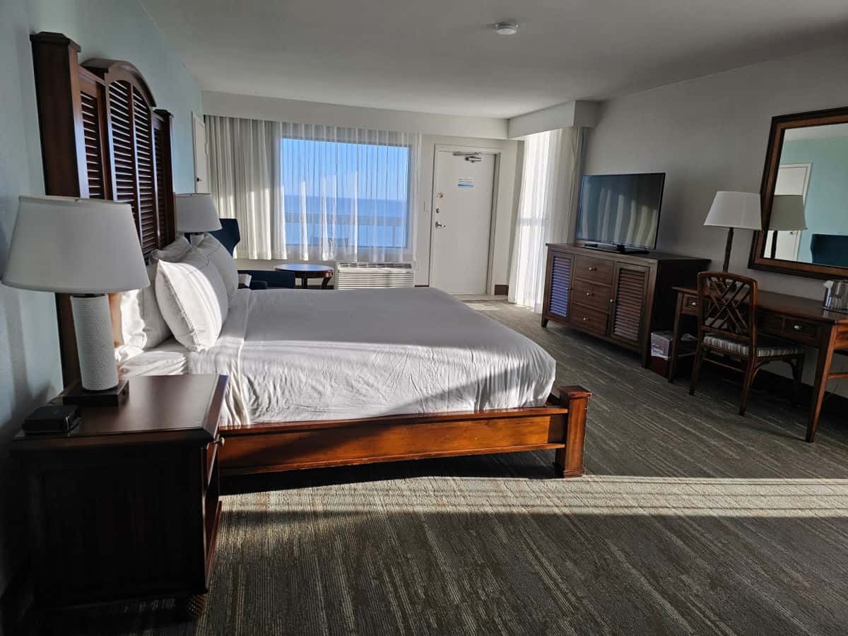 Large hotel room with king size bed, nightstands with lamps, window looking out over the water