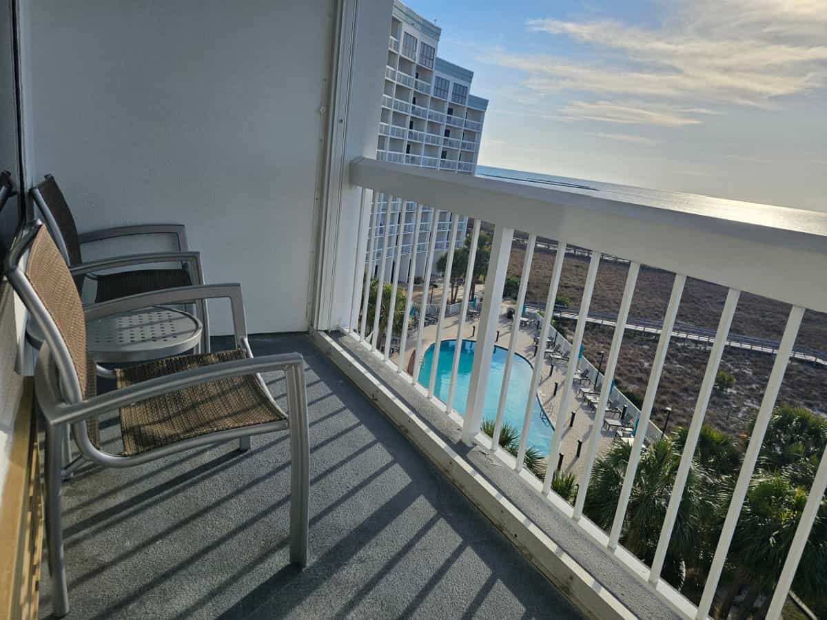 Balcony with two chairs, a small table looking over a pool and the Gulf of Mexico
