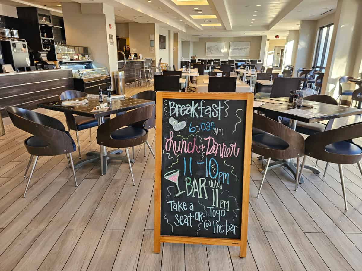 Hotel restaurant with breakfast lunch and dinner sign, tables and chairs in a bright room