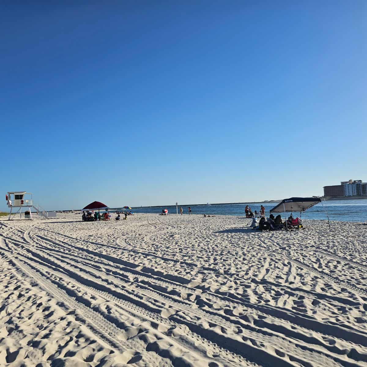 White sand with a lifeguard stand, people on the beach with tents