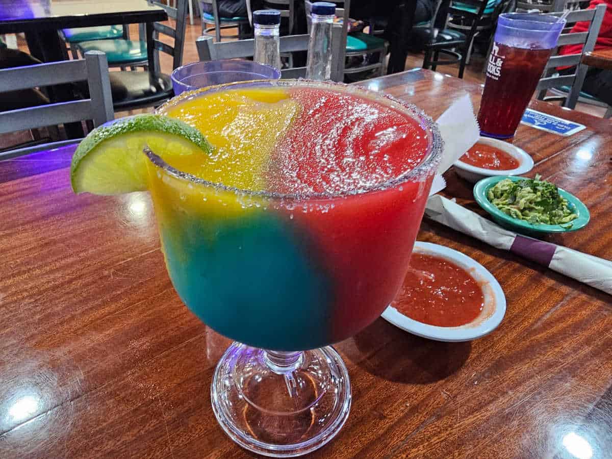 large rainbow margarita next to salsa and guacamole
